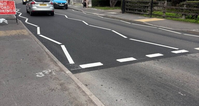 Freshly painted white road markings at a pedestrian crossing on a Sheldon road, showing give-way lines and lane dividers on new black asphalt, with a Road Markings sign visible